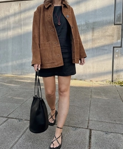 Détail d'une veste en daim marron à revers rétro portée avec un sac seau noir chic
