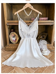 Détail d'une nuisette en satin blanc avec une applique en dentelle papillon sur le décolleté