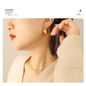 Close-up of a model wearing polished gold spherical C-shaped earrings and a thin chain