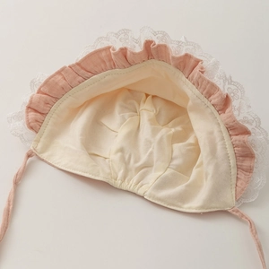 Dettaglio della cuffia rosa per neonati con pizzo floreale bianco e volant in cotone
