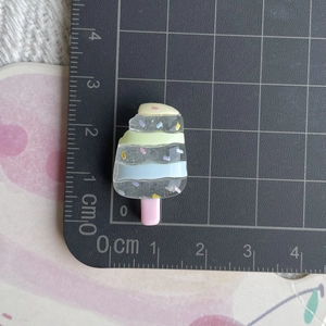 Vue macro de breloque glace en résine colorée avec mesures d'échelle sur tapis