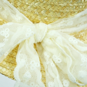 Detailed close-up of woven straw texture and floral lace ribbon on a summer beach hat