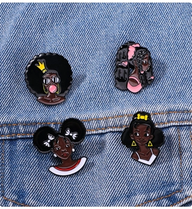 Detailed view of four cartoon black girl enamel pins pinned to a blue denim jacket pocket