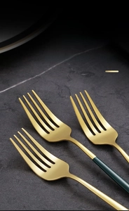 Detail of polished golden stainless steel forks with matte green handles on stone