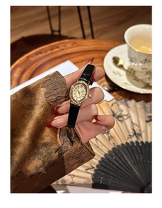 Close-up of vintage oval gold watch with diamond bezel and black leather strap on wrist