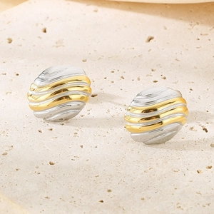 Détail macro de boucles d'oreilles ovales bicolores or et argent avec texture ondulée sur pierre