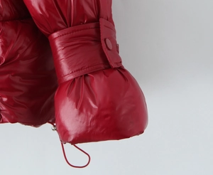 Detailed close-up of red shiny puffer jacket cuff with metallic finish and button detail