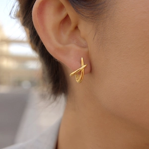 Detailed view of minimalist gold X-shaped cross earrings on model's ear
