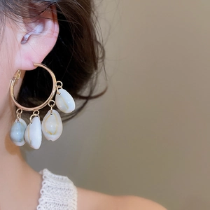 Detail of golden hoop earring featuring four natural white shell pendants in bohemian style