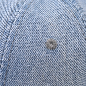 Detail of light blue denim fabric texture and embroidered eyelet on baseball cap crown