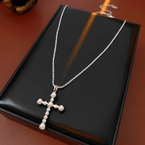 Détail macro du collier pendentif croix argenté avec perles métalliques sur support en cuir noir