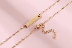Detail of gold horizontal bar necklace with a red gem inlay and heart engraving