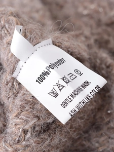 Close-up of a white care label on a brown knit sweater showing 100% polyester material