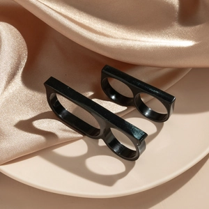 Detail of two black double-finger rings on beige satin fabric with soft lighting