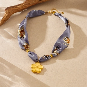 Detail of grey leopard print silk ribbon necklace with a golden floral pendant on sand