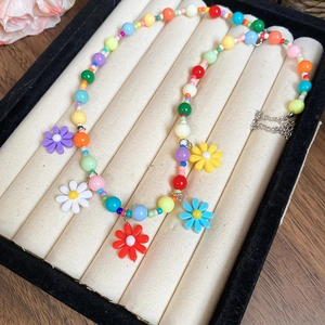 Detail showing colorful beaded necklace with daisy charms on a velvet jewelry tray