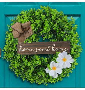 Detail of green artificial wreath with daisies and home sweet home sign on blue door