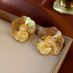 Macro detail of gold flower stud earrings with sparkling crystal center and textured petals