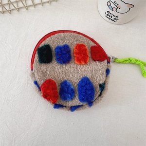 Close-up of plush round mini bag with colorful patches and green woven lanyard