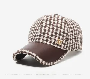 Detail of houndstooth baseball cap with golden M logo and brown faux leather brim