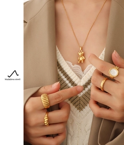 Close-up of golden bear pendant necklace and assorted rings on a model with blazer