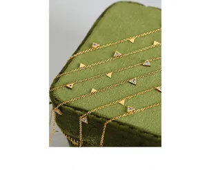 Macro detail of 18K gold triangle necklace with zircons on green velvet box