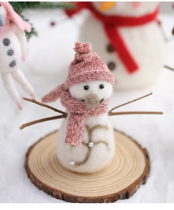 Close-up of handmade wool felt snowman with pink knit hat and scarf on wood base
