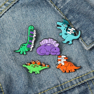 Detail of five cute cartoon dinosaur enamel pins on denim background for student style