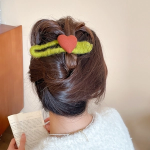 Detail of green knit hair clip with red heart worn on a bun for casual styling