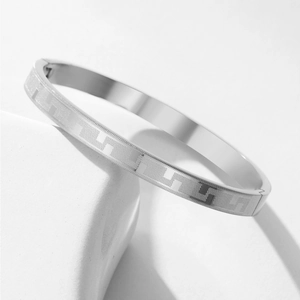 Detailed view of silver stainless steel bangle with geometric fret pattern on stone base