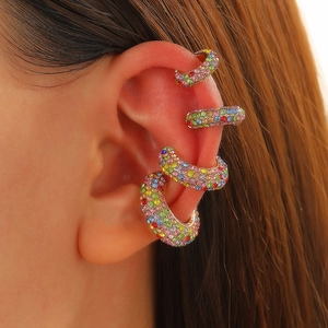 Detail of four colorful rhinestone ear cuffs in gold finish worn on the ear cartilage