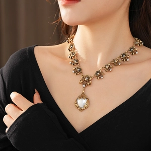 Détail d'un collier vintage doré à fleurs avec strass et perle blanche au cou