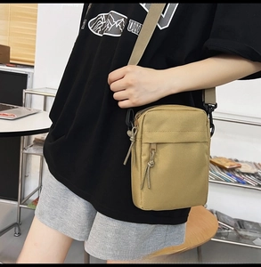 Detail showing the khaki nylon crossbody bag with dual zippered pockets and woven pulls