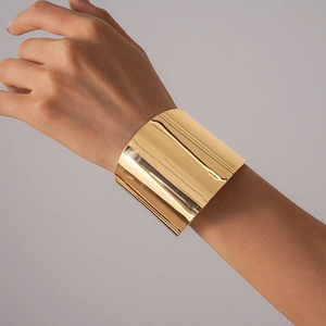 Gros plan d'un large bracelet manchette en métal doré poli sur le poignet d'un mannequin