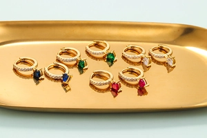 Golden heart hoop earrings with colorful zircon stones on an elegant metal tray