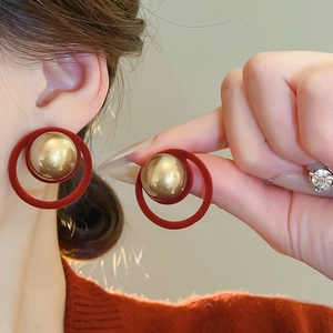Close-up of geometric earrings featuring red flocked rings and polished gold metal balls