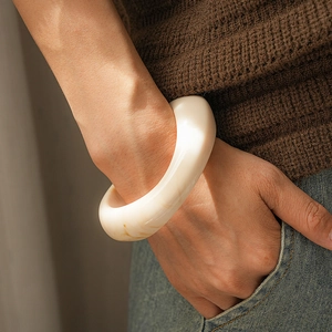 Close-up of a wide cream resin cuff bracelet with brown marble texture on a model