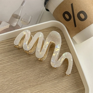 Macro detail of wave-shaped acetate hair claw clip with white marble texture and gold claws