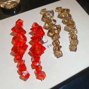 Detail view of long chunky acrylic earrings in orange and amber faceted geometric beads