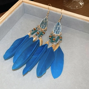 Detail of bohemian drop earrings with blue feathers and colorful beads on a tray