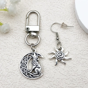 Detail view of antique silver moon and wolf pendant keychain with sun earring on texture