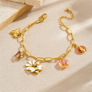 Golden charm bracelet with enamel bees flowers and ladybugs on a textured stone background