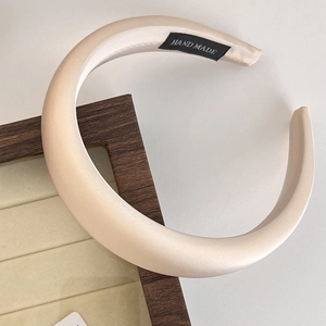 Close-up of beige padded satin headband with HAND MADE label on a wooden stand