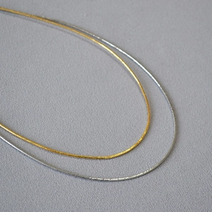 Dettaglio di girocollo a molla minimalista in oro e argento su sfondo materico raffinato