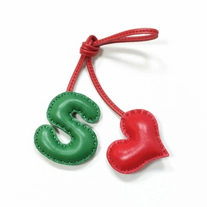 Close-up of handmade leather bag charm featuring green letter S and red heart with stitching
