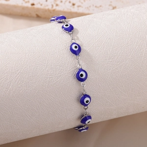 Detail shot of silver chain bracelet with blue evil eye enamel charms on white stand