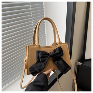 Detail of tan handbag with black bow decoration held against a grey shutter background