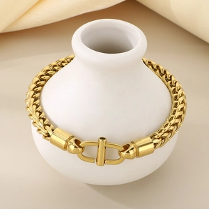 Détail du bracelet chaîne en or avec boucle en forme de D exposé sur un vase en céramique