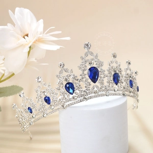 Detailed view of silver crown with blue teardrop rhinestones on white display stand