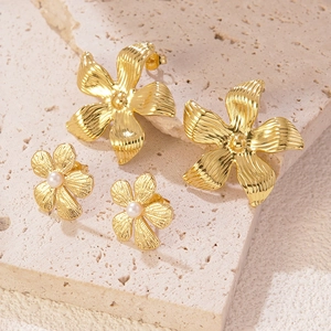 Elegant gold flower stud earrings with pearl centers on natural stone background